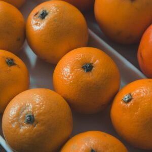 A detailed view of fresh oranges and persimmons in a white tray.